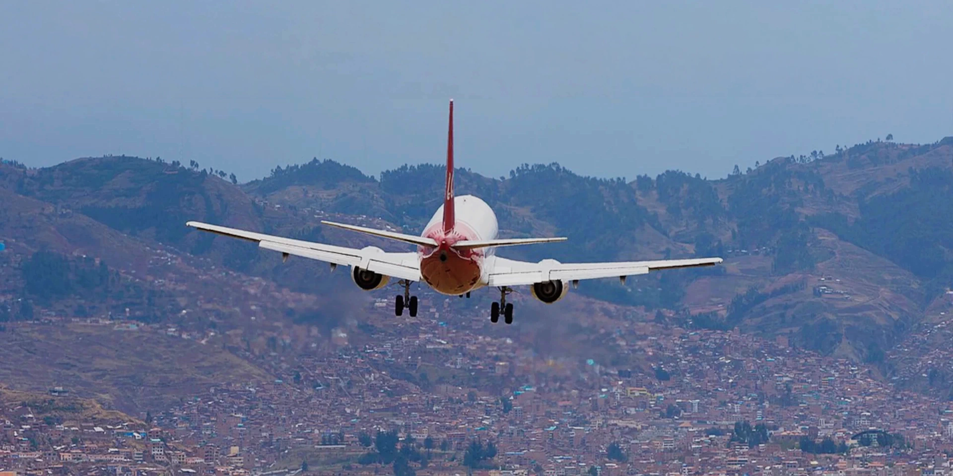 Rear view of a commercial airplane landing at Cusco airport with the sprawling city and Andean mountains in the background.
