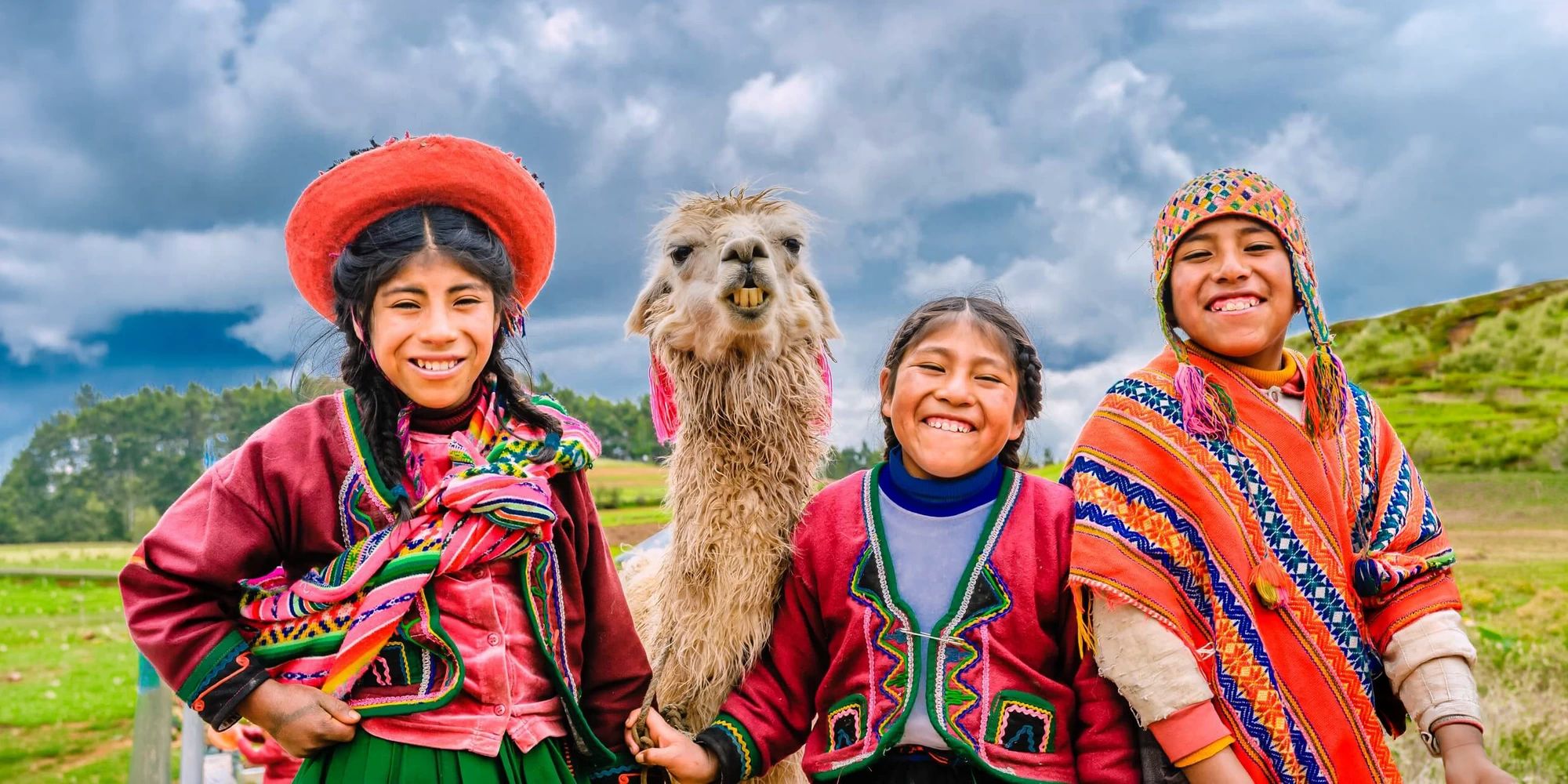 Landscape view of indigenous Peruvian children wearing traditional hand-woven clothes posing with an alpaca in the Andes.