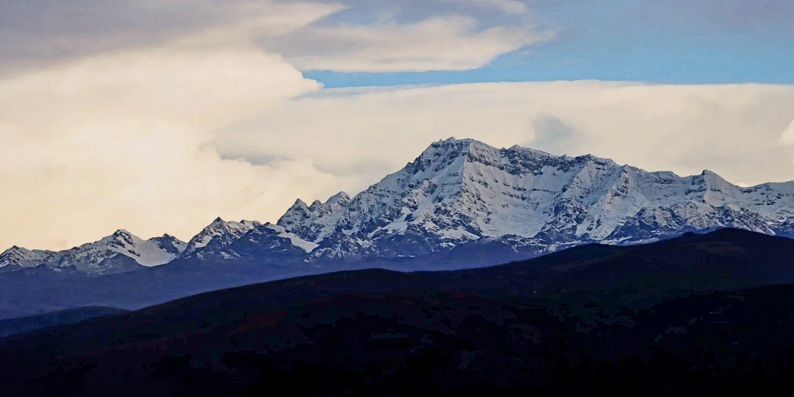 A beautiful silhouette of the snow-covered Andean mountain range at dusk with soft clouds.