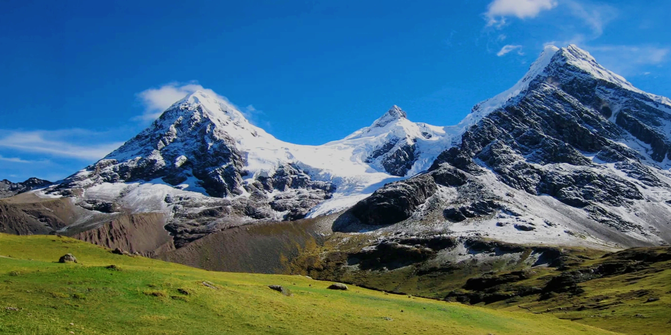 Panoramic view of snow-capped Andean peaks and green highlands under a blue sky in Cusco, Peru.