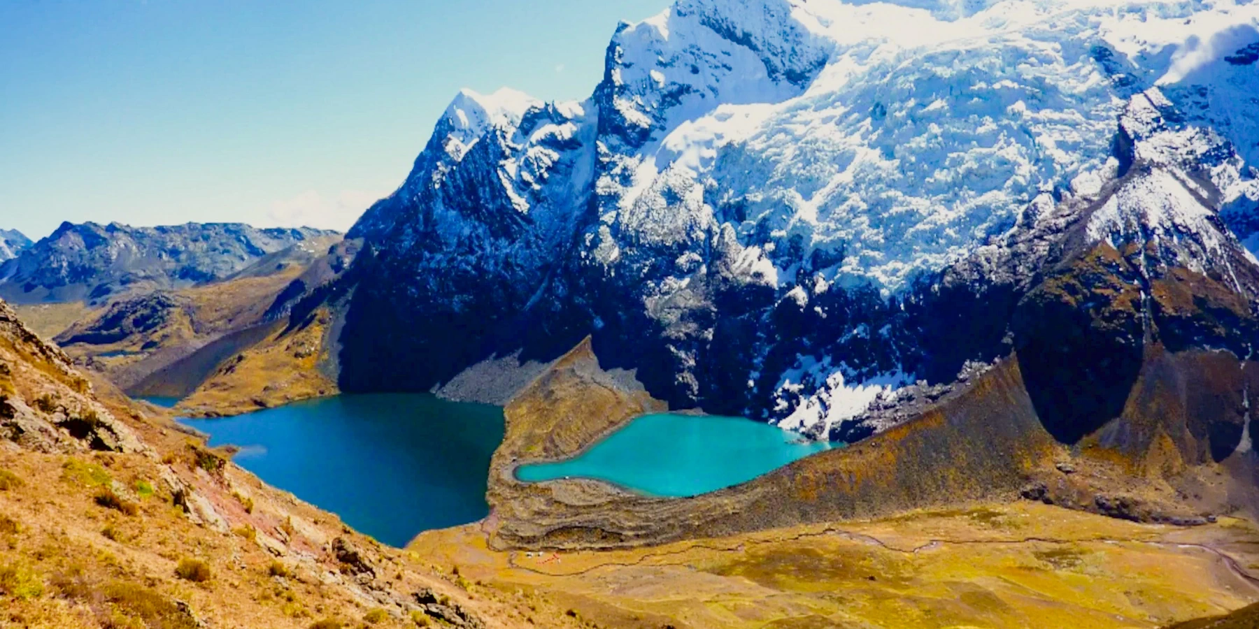 Panoramic view of two turquoise glacial lakes at the foot of the snow-capped Ausangate mountain in Peru.