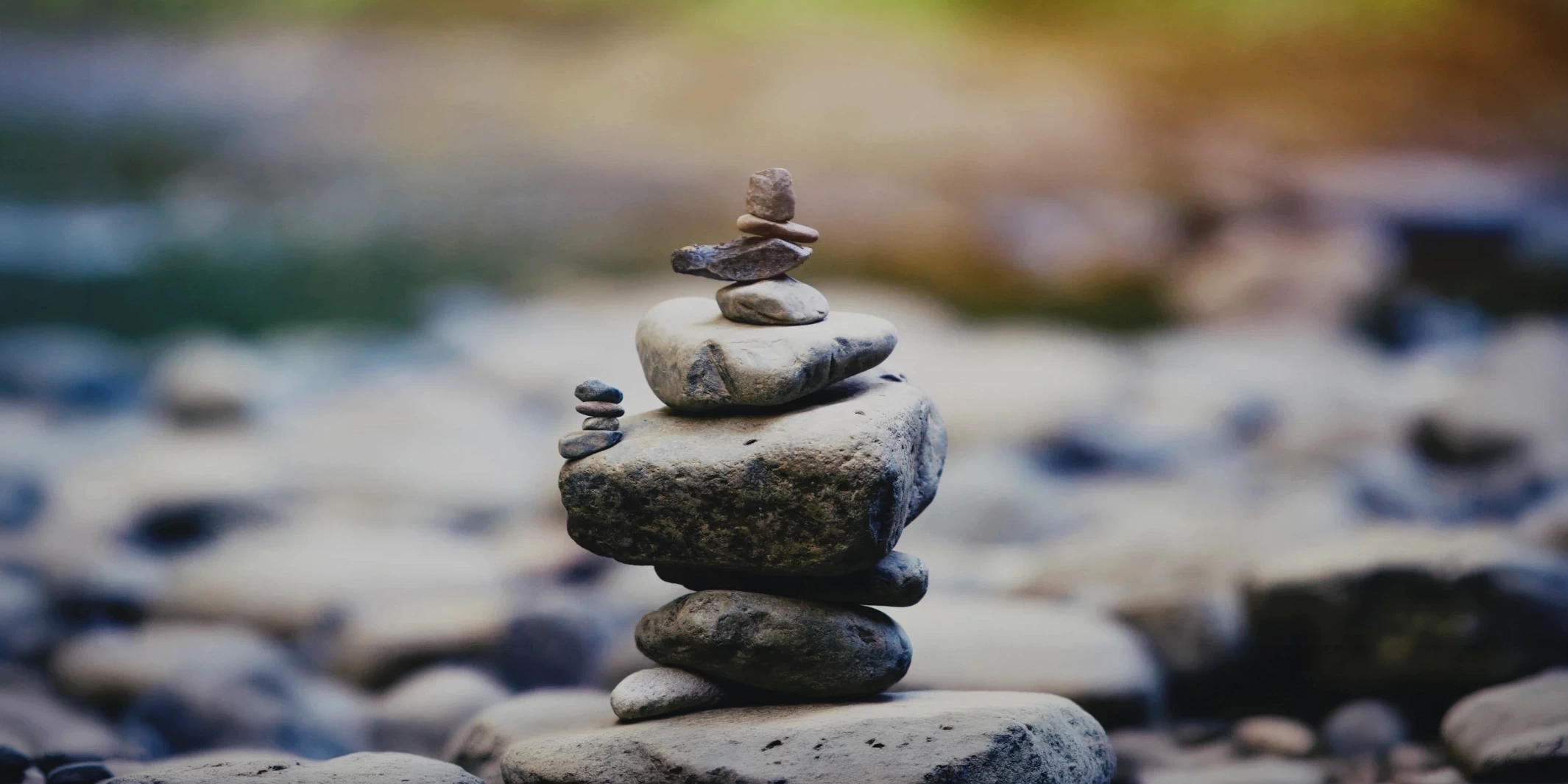 A stack of balanced stones, known as apachetas, on a riverbank with a blurred natural background.