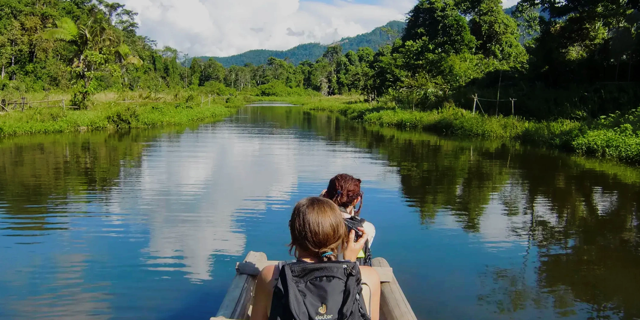 Two tourists enjoying a peaceful canoe ride through a narrow river in the heart of the Amazon rainforest.