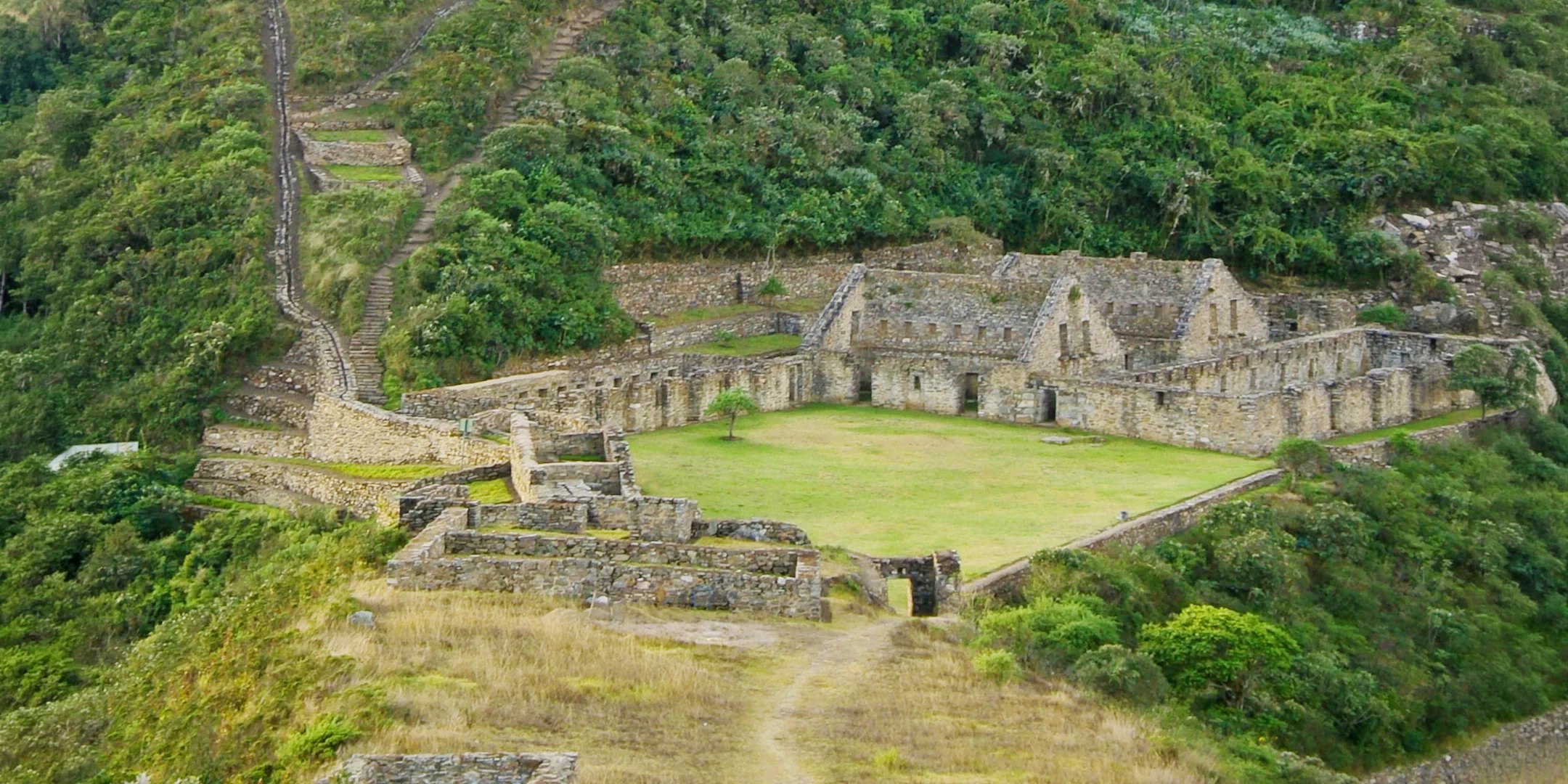 Overview of the Choquequirao main plaza and surrounding agricultural terraces on a lush hillside.