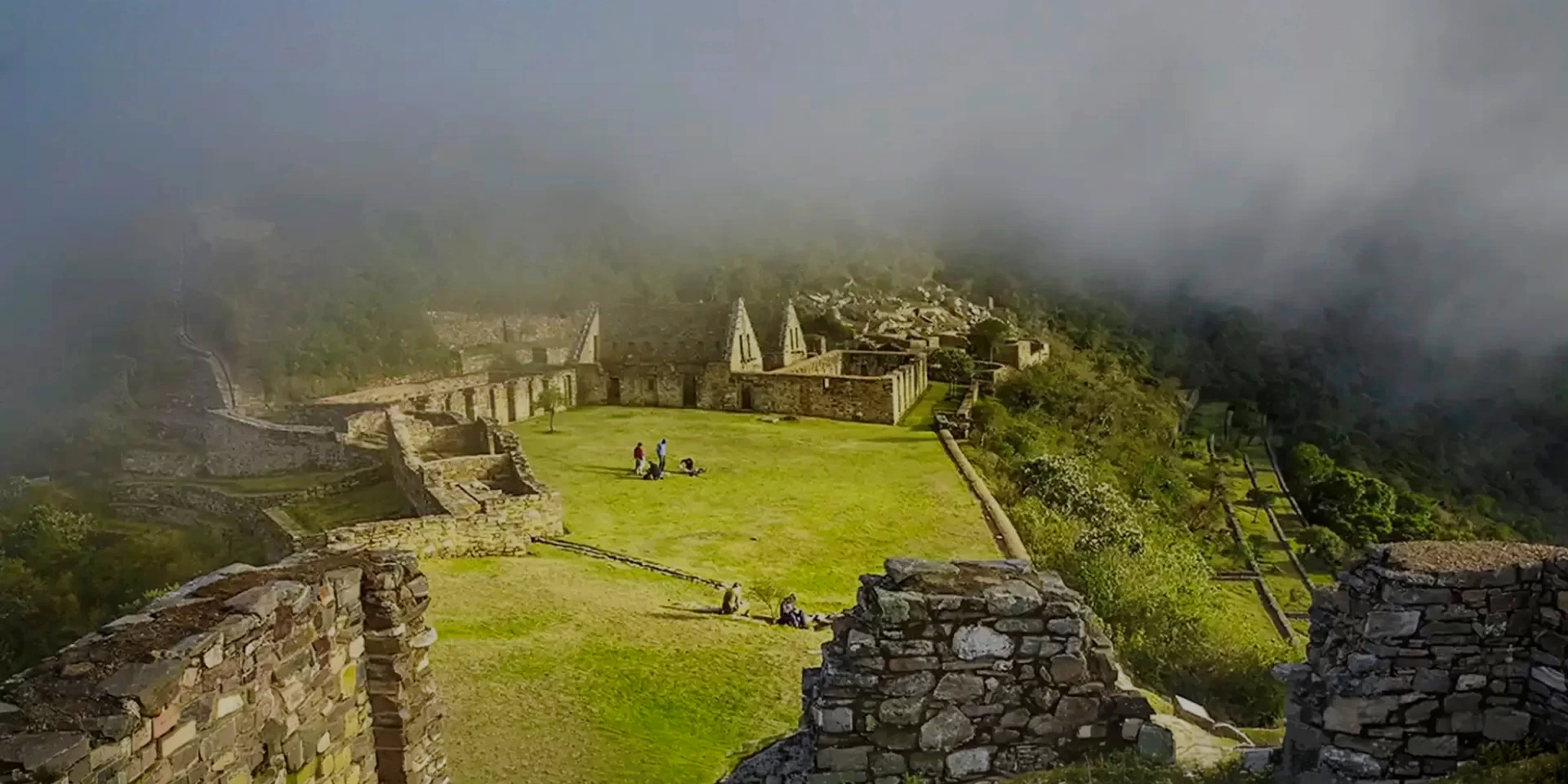 The main plaza of Choquequirao partially covered by clouds and mist, creating a mystical atmosphere in the high-altitude Peruvian Andes.