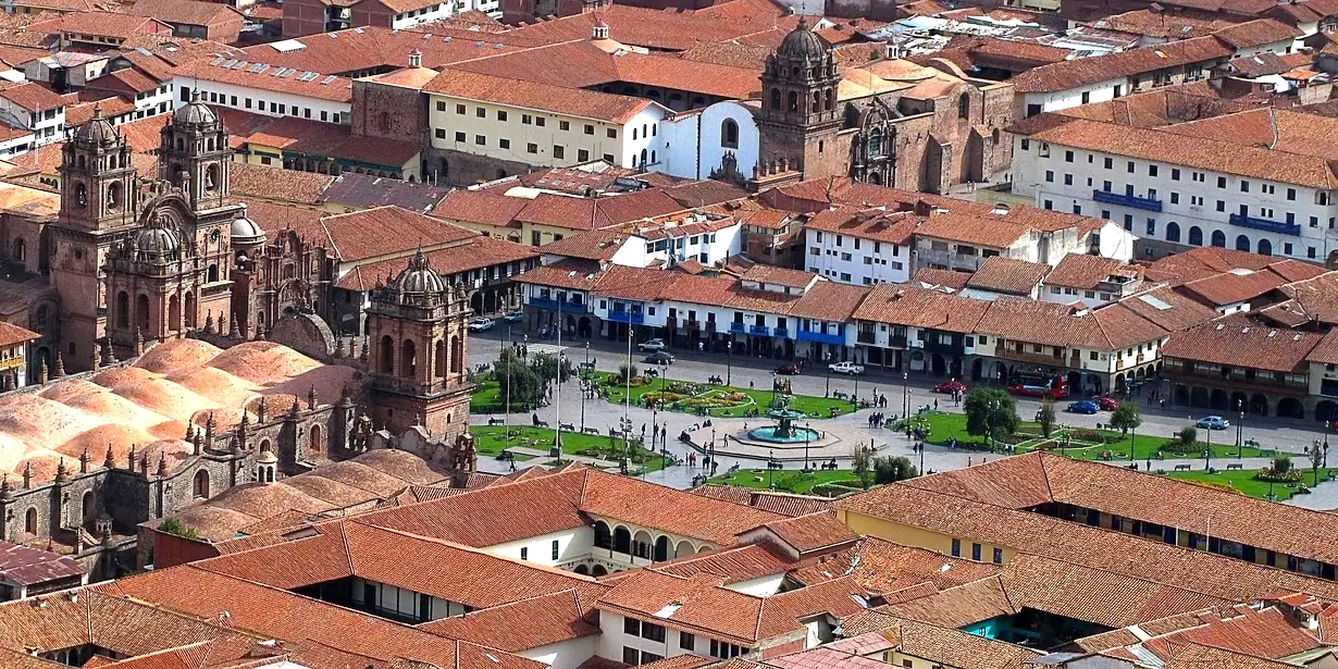 Aerial panoramic view of Cusco's Plaza de Armas, showing the Cathedral, La Compañía church, and red-tiled roofs.