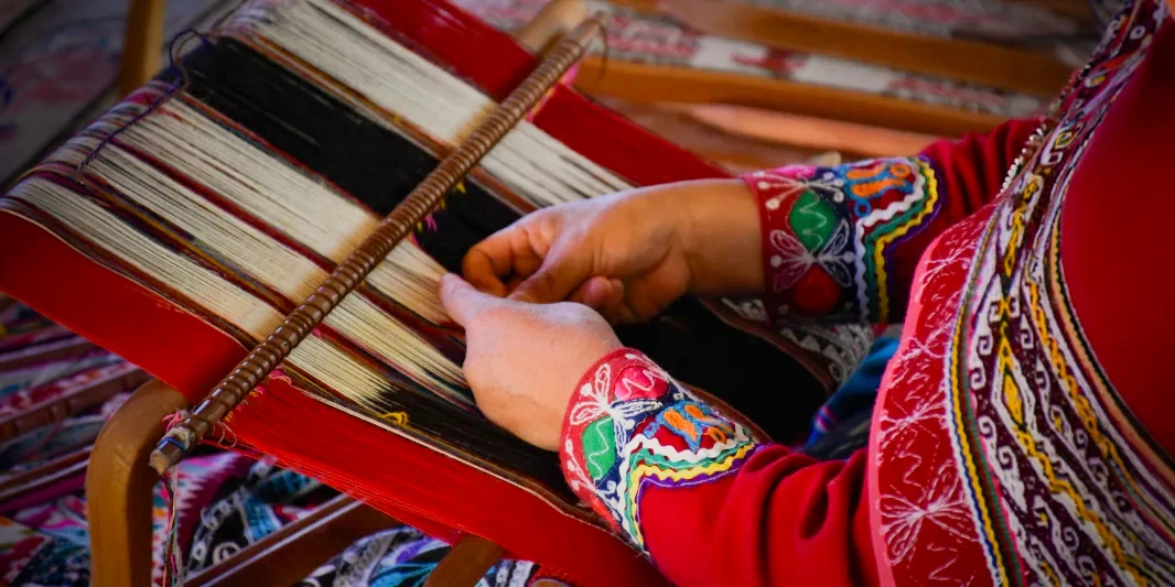 Extreme close-up of a weaver's hands working on a traditional red and white textile using a wooden loom.
