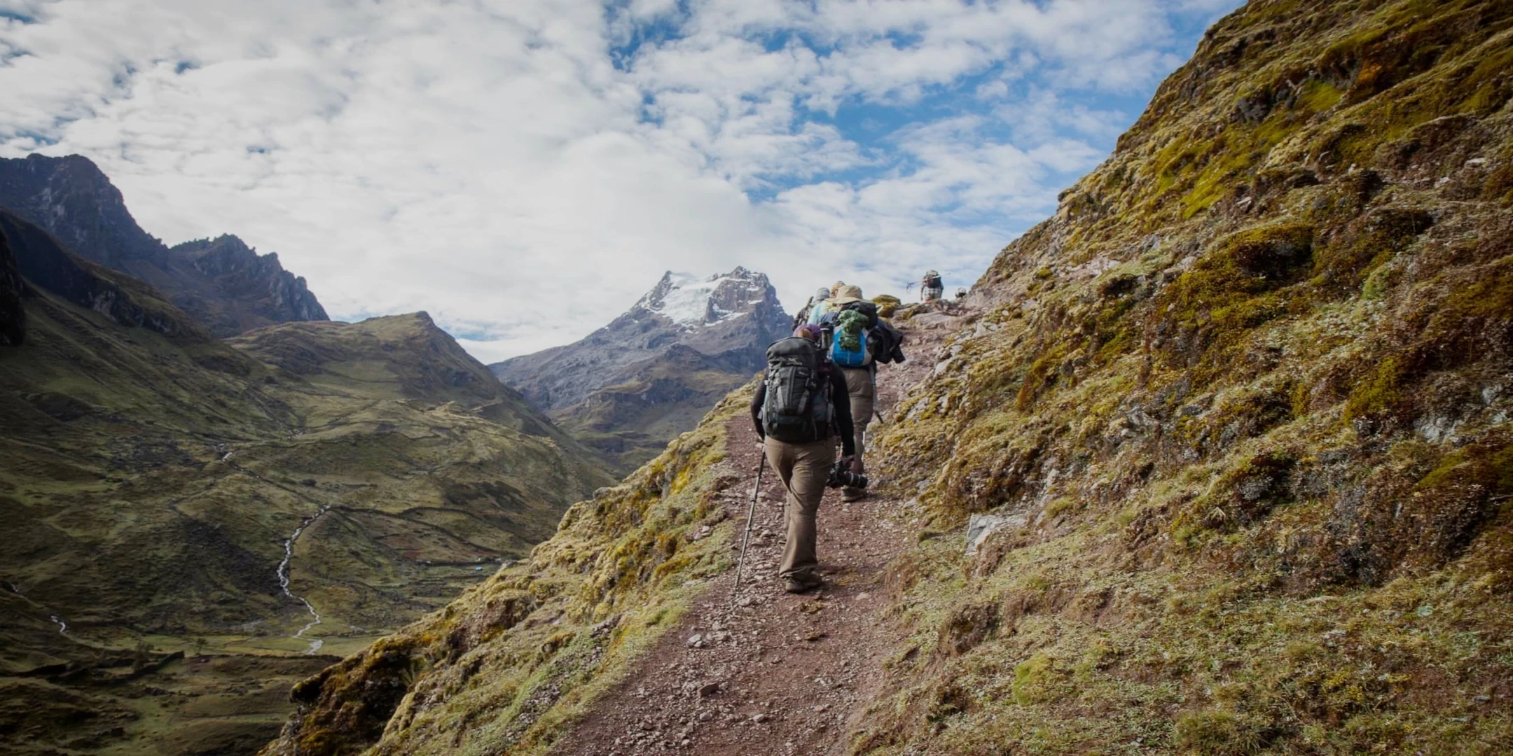 Ancient stone agricultural terraces on a steep green slope with mountains partially covered by clouds in the background.