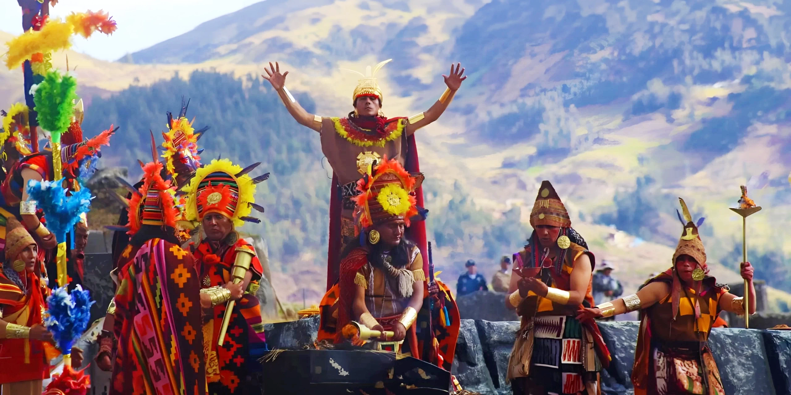 Large scale reenactment of an Inca ceremony at Sacsayhuaman with performers in vibrant traditional costumes and mountains in the background.