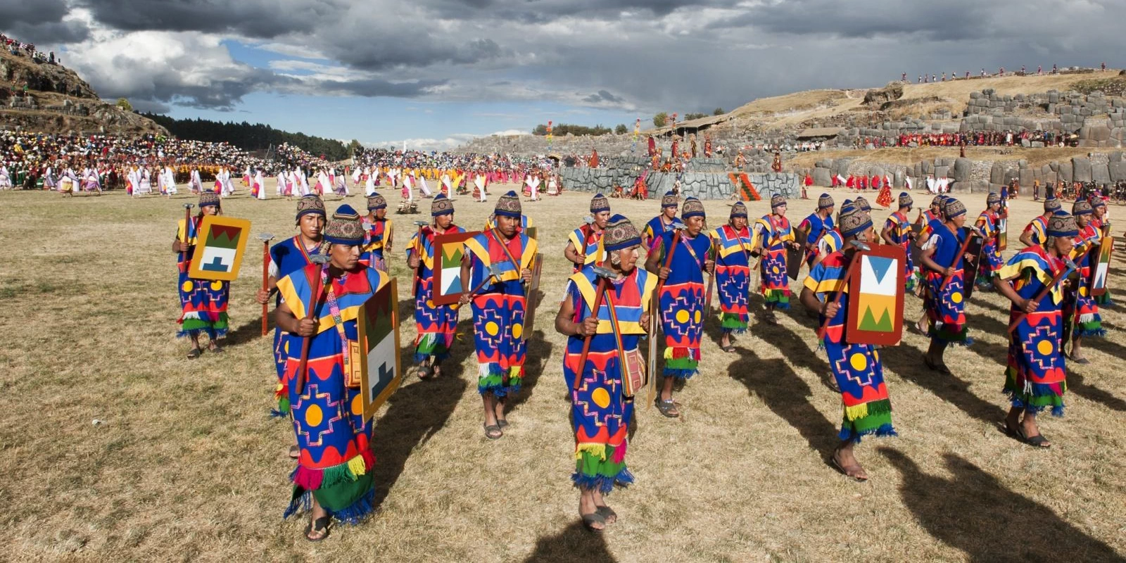 Incan warriors in traditional blue and red tunics carrying shields during the Inti Raymi ceremony at Sacsayhuaman.