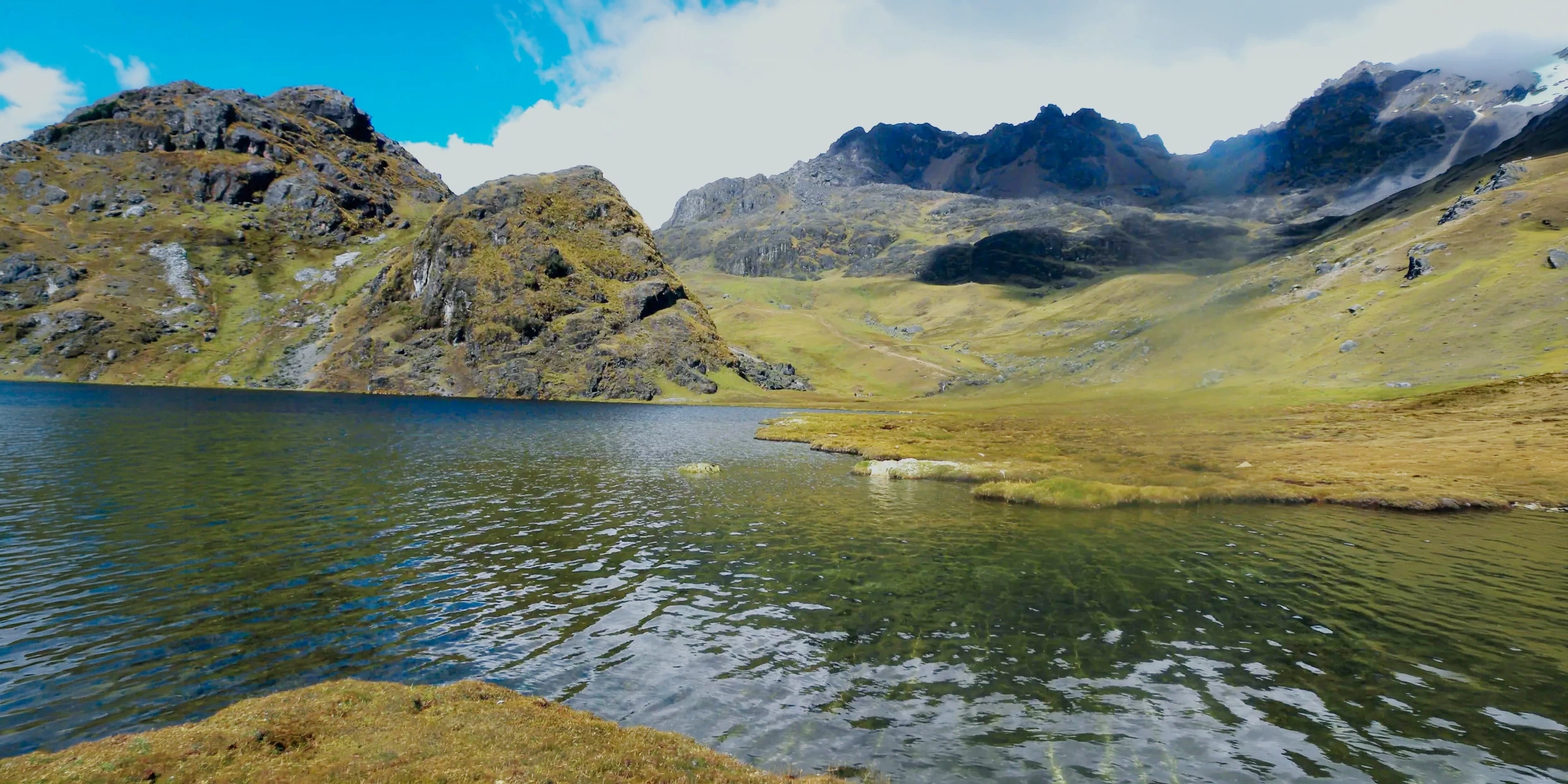 A serene blue lake surrounded by rugged mountains and green slopes on the Lares Trek.