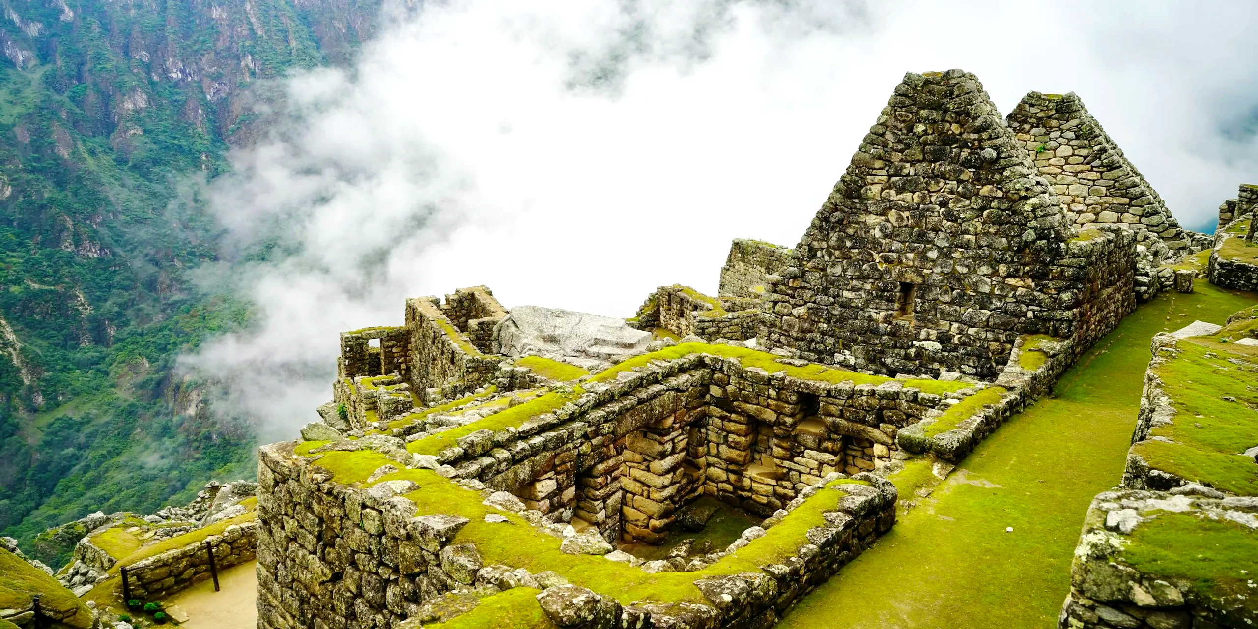 Panoramic view of the stone ruins of Machu Picchu surrounded by mystical clouds and green mountains.