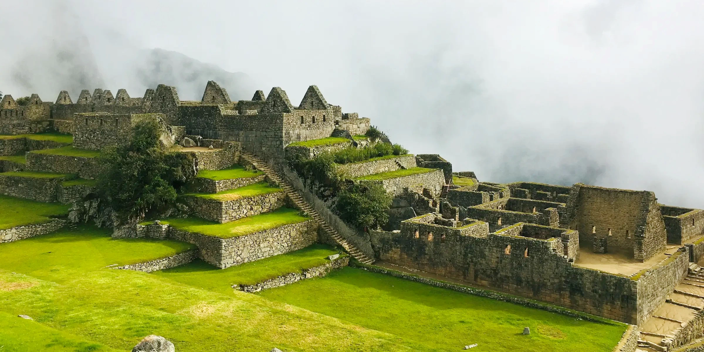 Panoramic view of the stone structures and terraces at the Machu Picchu sanctuary under a cloudy sky.