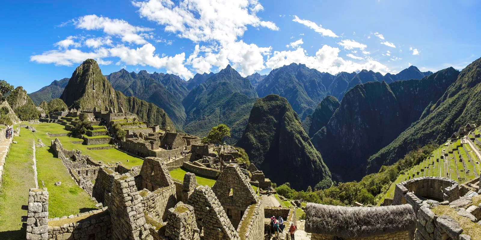 Wide shot of the stone ruins of Machu Picchu city with mountains and clouds in the distance.