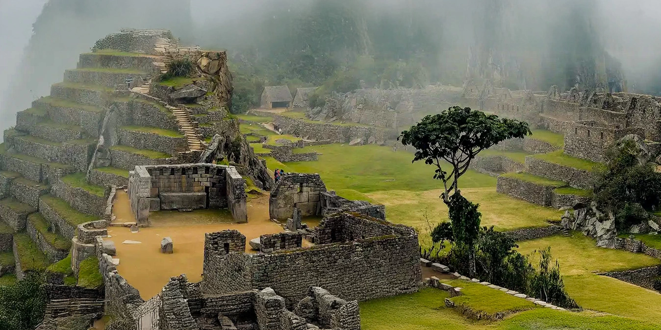Wide view of the urban sector and residential ruins of Machu Picchu with fog-covered mountains in the background.