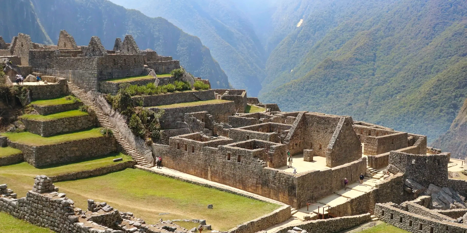 Stone structures and agricultural terraces at the Machu Picchu archaeological site with mountains in the background.