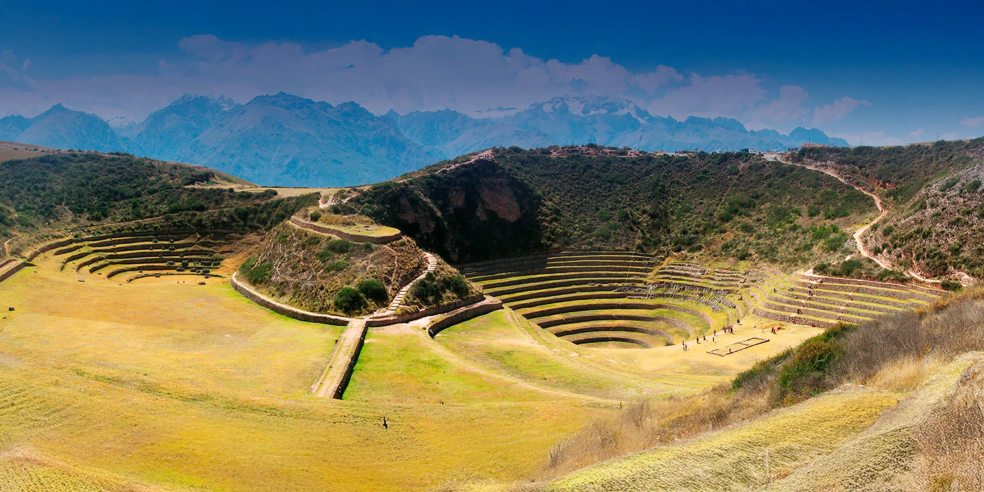 Vibrant view of the Moray circles against a deep blue sky and the high peaks of the Sacred Valley.
