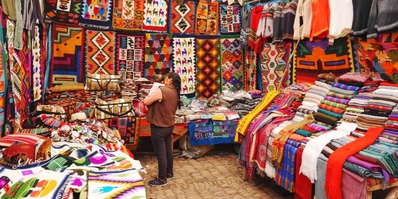 A vibrant display of traditional Andean blankets and textiles with geometric patterns and llama motifs in a Cusco craft market.
