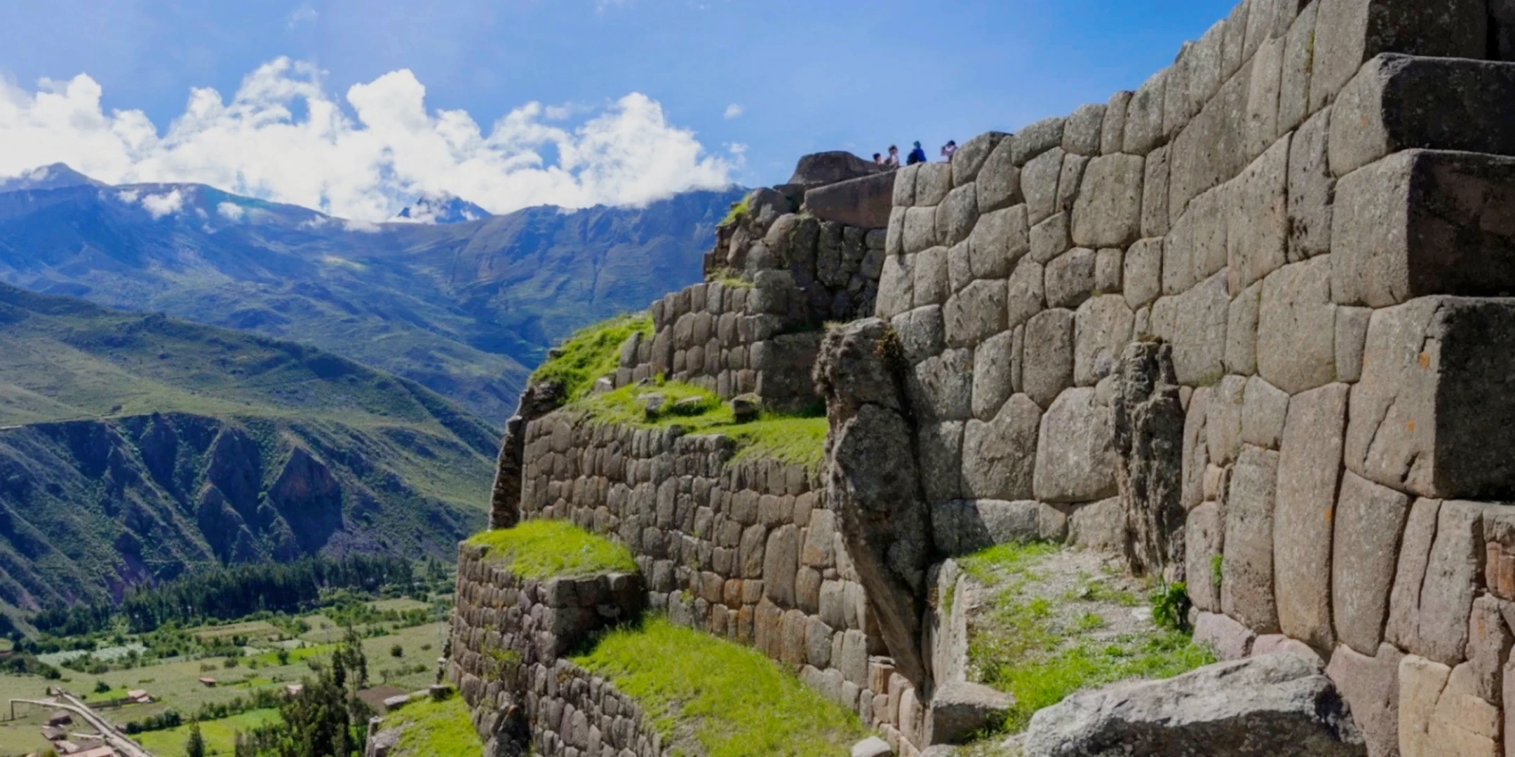 Massive Inca stone walls at the Ollantaytambo archaeological site with a view of the green valley and mountains.