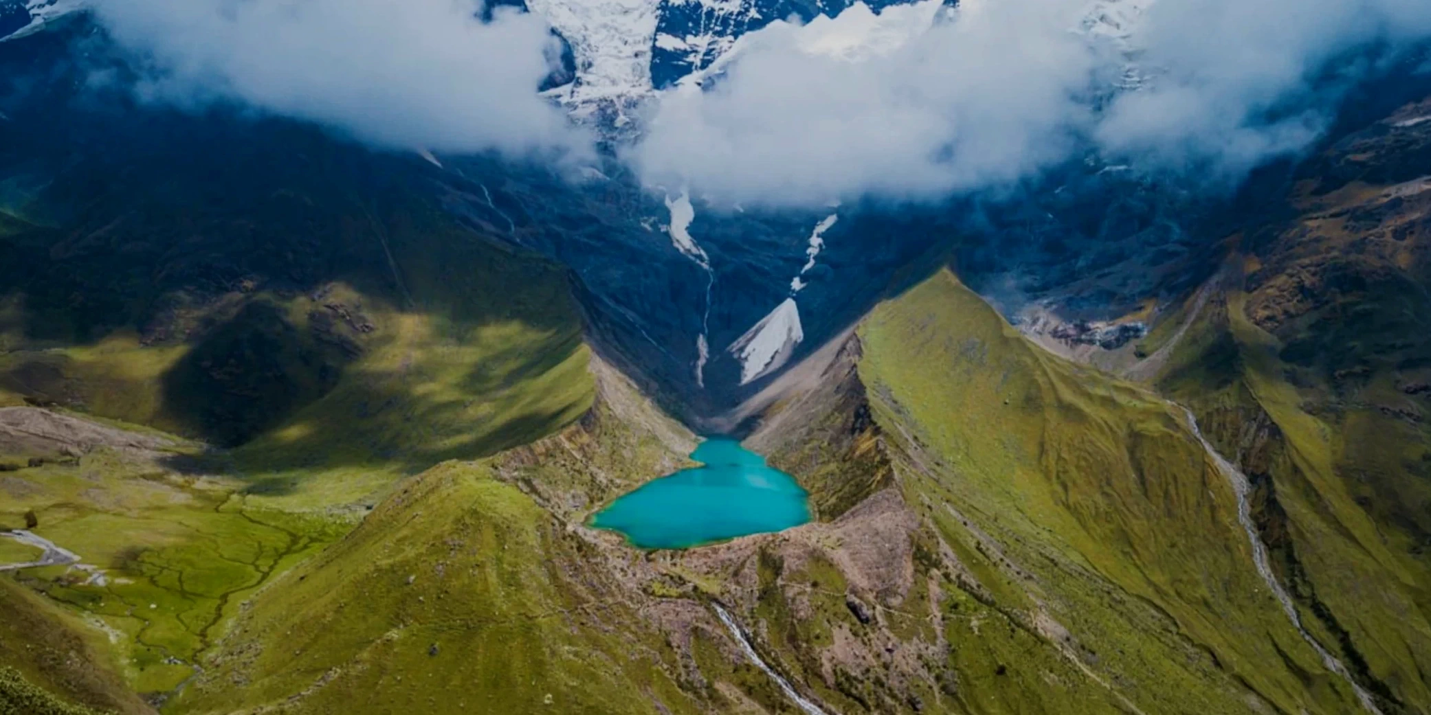 Panoramic view of the turquoise Humantay Lake nestled between green mountain ridges and a white glacier.
