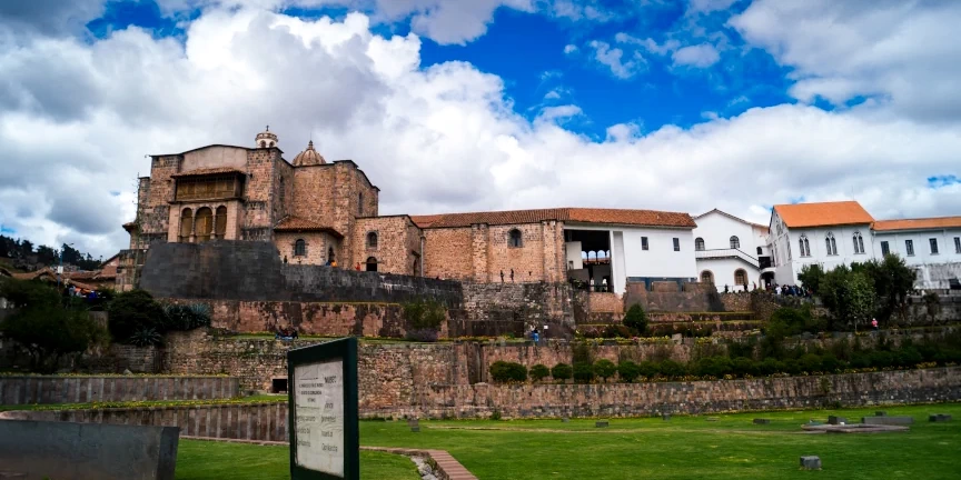 Panoramic exterior view of the Qorikancha Temple and Santo Domingo Convent with green gardens under a blue sky in Cusco.
