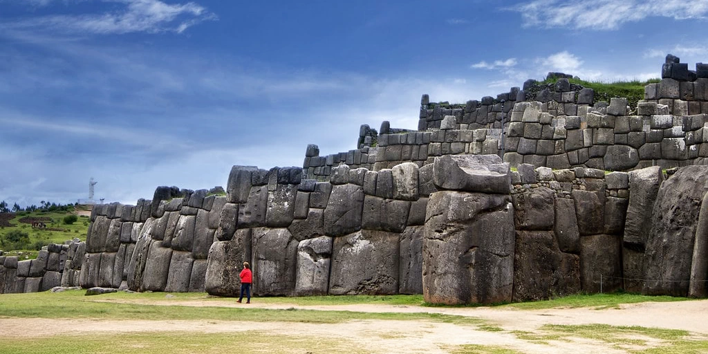 Massive zigzagging stone fortifications at the Sacsayhuaman archaeological site under a blue sky.