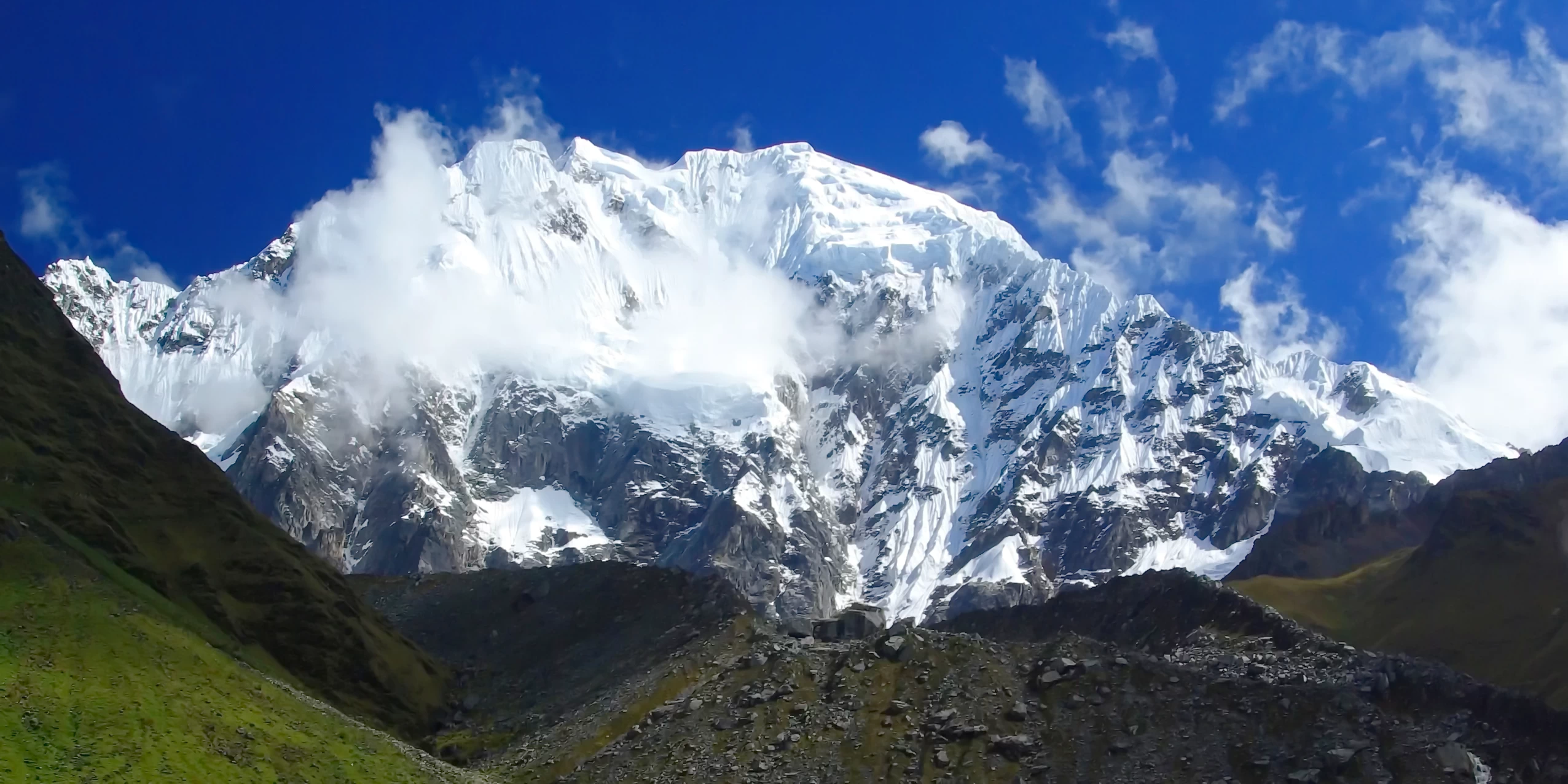 Close-up of the majestic snow-covered Salkantay mountain peak with white clouds and blue sky.