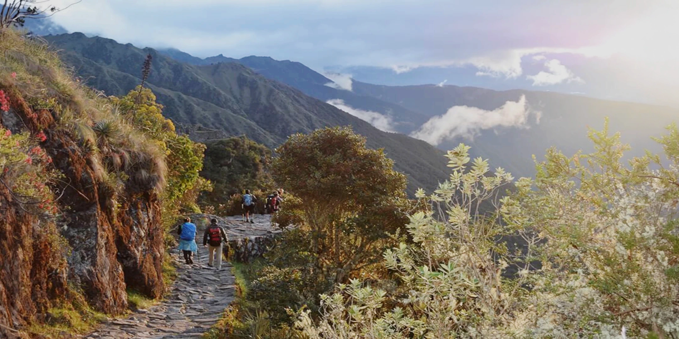 A group of hikers walking along the original stone path of the Short Inca Trail during a golden sunset with mountain views.