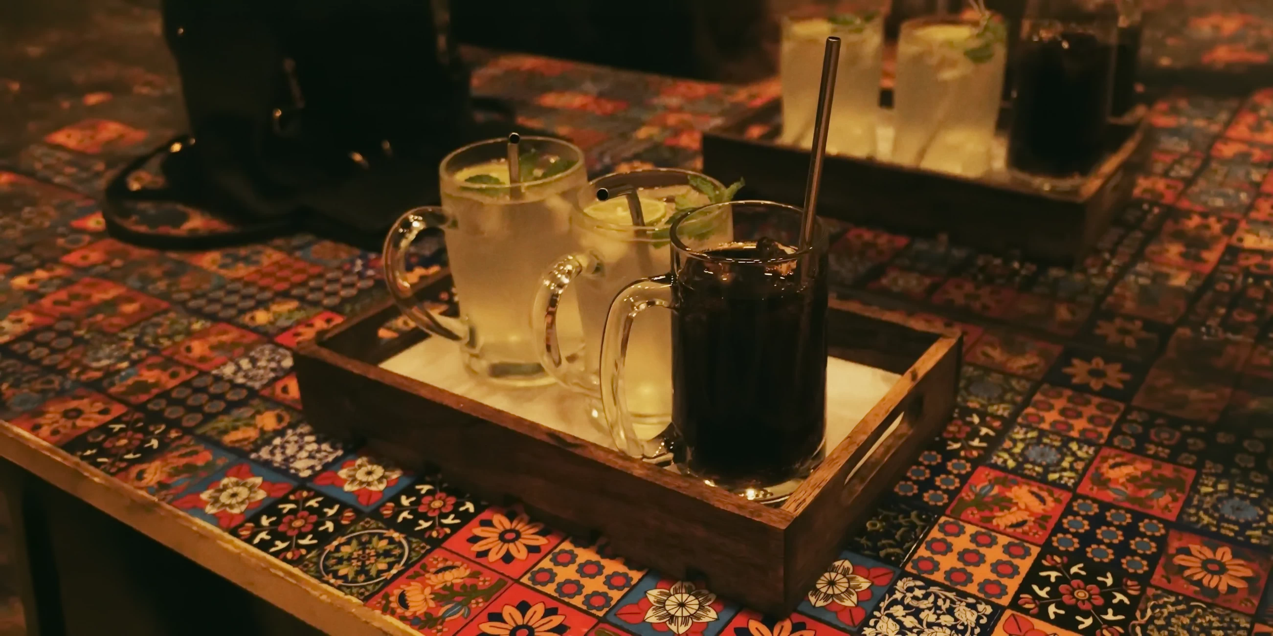 A wooden tray with different traditional Peruvian drinks served on a colorful patterned tablecloth.
