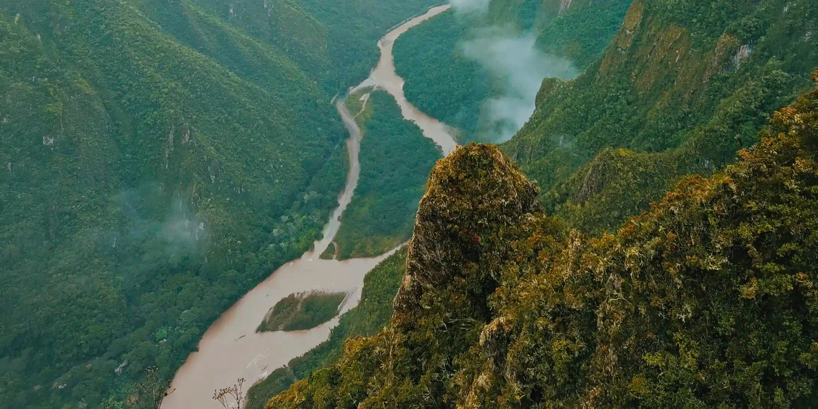 Aerial panoramic view of the Vilcanota River winding through the lush green mountains of the Sacred Valley near Machu Picchu.