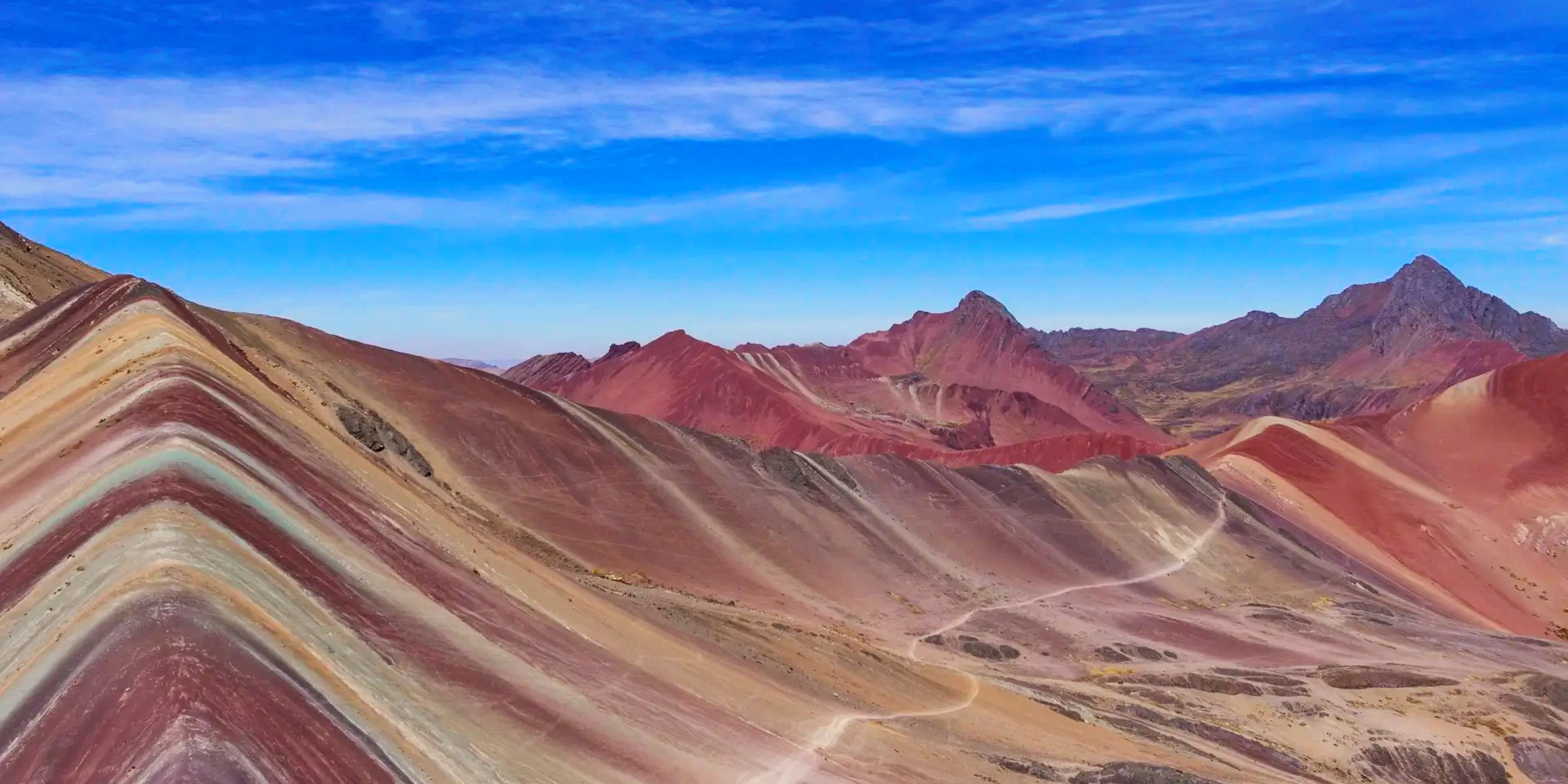 Wide landscape of the vibrant mineral stripes of Rainbow Mountain against a bright blue sky in the Peruvian Andes.