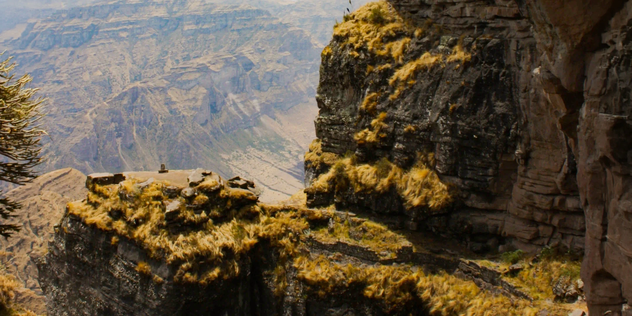 Wide landscape view of the rugged mountains and ancient ruins of Waqrapukara seen from a rocky overlook.