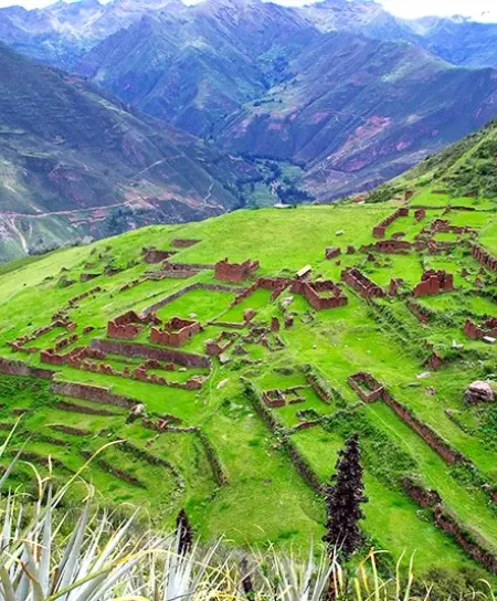 High-angle view of the Huchuy Qosqo stone structures and green terraces overlooking the deep canyons of the Sacred Valley.