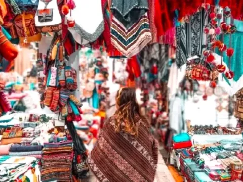 A traveler wearing a traditional poncho browsing through colorful Andean textiles and handmade wool clothing at the local market
