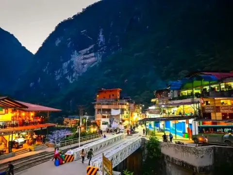 Night view of Aguas Calientes with glowing lights on the bridge and Andean mountains in the background
