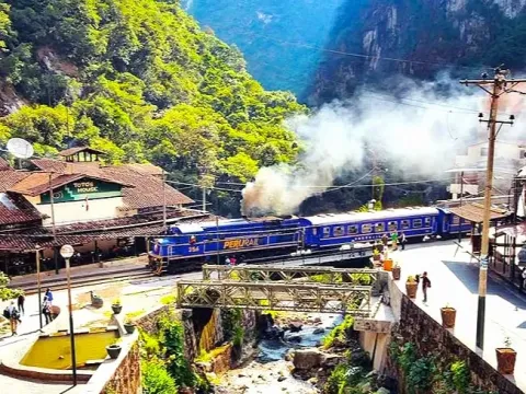 PeruRail blue train arriving at Aguas Calientes station, Peru, with jungle mountains and river