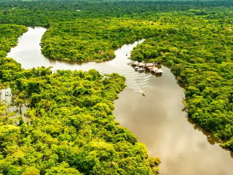 Aerial view of eco-lodges and traditional floating houses along a wide river in the Peruvian Amazon.