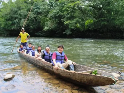A group of tourists in life jackets enjoying a guided tour in a traditional wooden canoe on a jungle river.