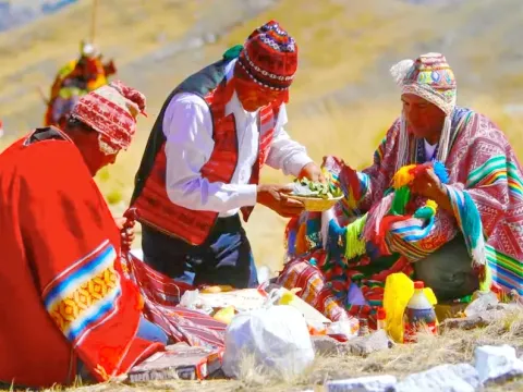 Three people in traditional Cusco attire performing a "Pago a la Tierra" ceremony with coca leaves and sacred elements on the ground.Three people in traditional Cusco attire performing a "Pago a la Tierra" ceremony with coca leaves and sacred elements on the ground
