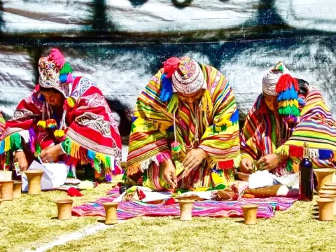 A group of Andean shamans sitting in a row on a colorful textile, wearing traditional ponchos and chullos during a spiritual ritual