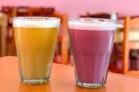 Two glasses of traditional Peruvian drinks: yellow Chicha de Jora and pink Frutillada.
