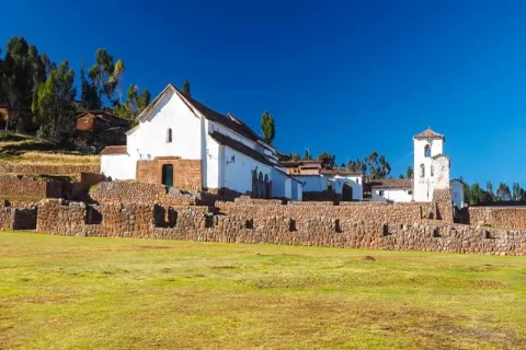 The white colonial church of Chinchero built upon ancient Inca stone foundations under a bright blue sky in the Sacred Valley.