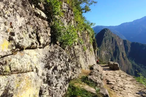 A narrow stone hiking path on the original Inca Trail with a view of Huayna Picchu mountain in the background.