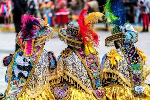 Close-up of three people wearing intricately decorated traditional Andean hats with colorful feathers.