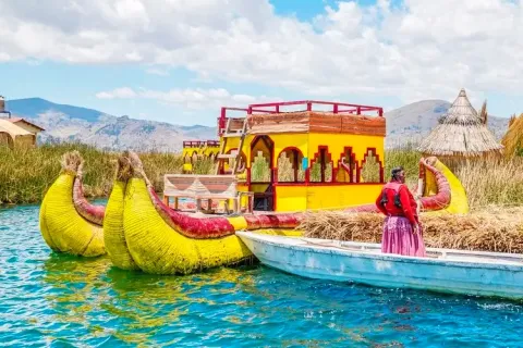 Brightly painted yellow and red traditional reed boats docked at a floating island in Lake Titicaca with a local woman in the foreground.