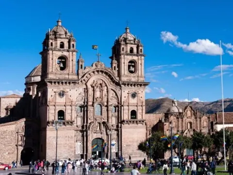 The Cusco Cathedral and the flag of Cusco flying in the Plaza de Armas under a blue sky