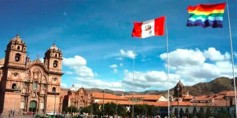 Seven-striped Cusco flags and Peruvian flags flying in the Plaza de Armas, with colonial architecture in the background