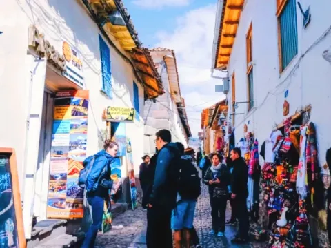 Narrow traditional street in Cusco with tourists walking past shops selling colorful Peruvian textiles and souvenirs