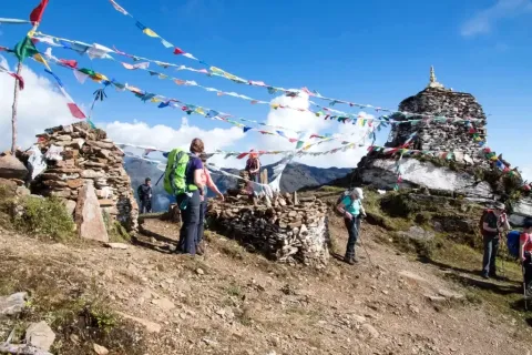 Group of trekkers standing near traditional Buddhist prayer flags and stone stupas on the Druk Path Trek in Bhutan.