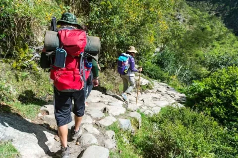 Hikers with backpacks walking on the ancient stone path of the Inca Trail to Machu Picchu, Peru.